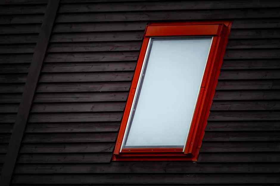 Close-up of a skylight with a red frame embedded in a dark wooden rooftop.